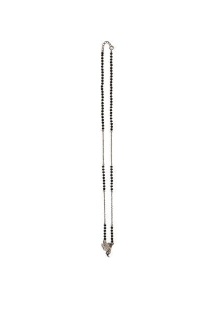 A delicate silver-toned chain necklace with small black beads, laid flat on a plain beige background.

