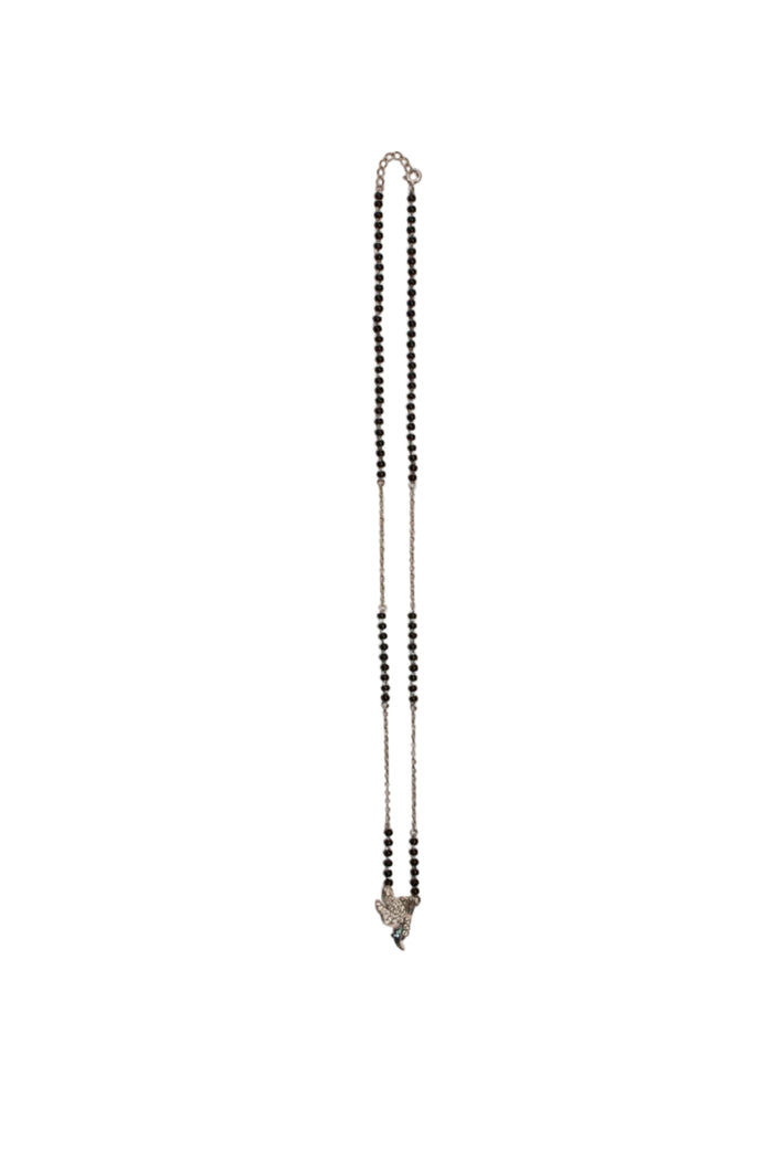 A delicate silver-toned chain necklace with small black beads, laid flat on a plain beige background.

