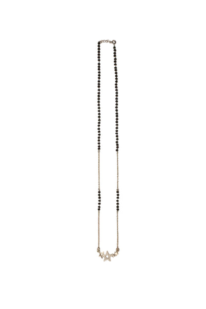 A delicate silver-toned chain necklace with small black beads, laid flat on a plain beige background.


