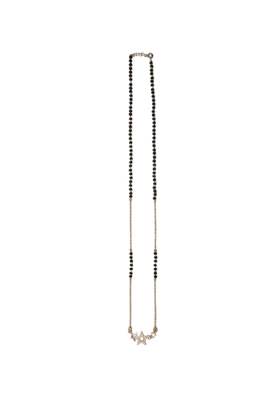 A delicate silver-toned chain necklace with small black beads, laid flat on a plain beige background.

