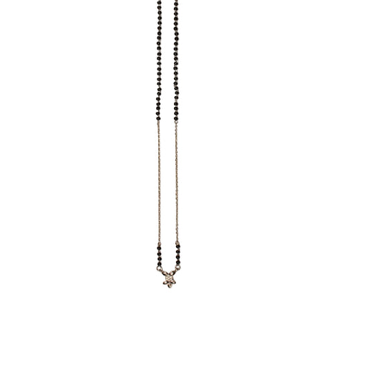 A delicate beaded necklace with small black beads on a fine silver chain, laid flat on a light beige background.